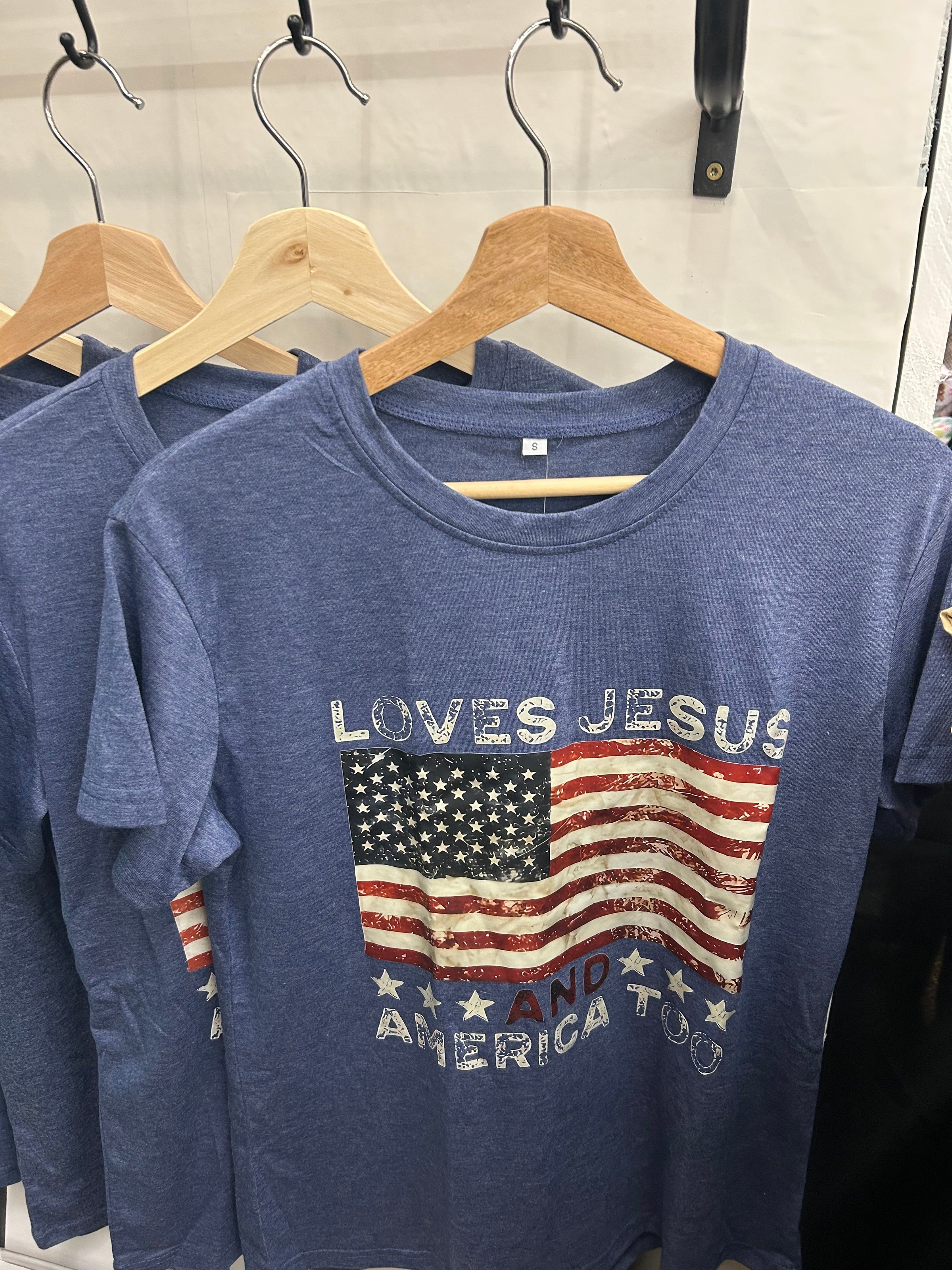 Blue t-shirt with rounded color with words loves Jesus with America too below united states flag